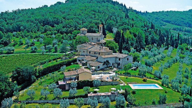 Una villa en la ladera con piscina, jardines escalonados y una torre de iglesia.