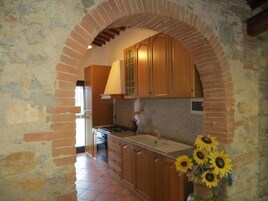 Una cocina con armarios de madera, un arco de ladrillo y un jarrón con girasoles.