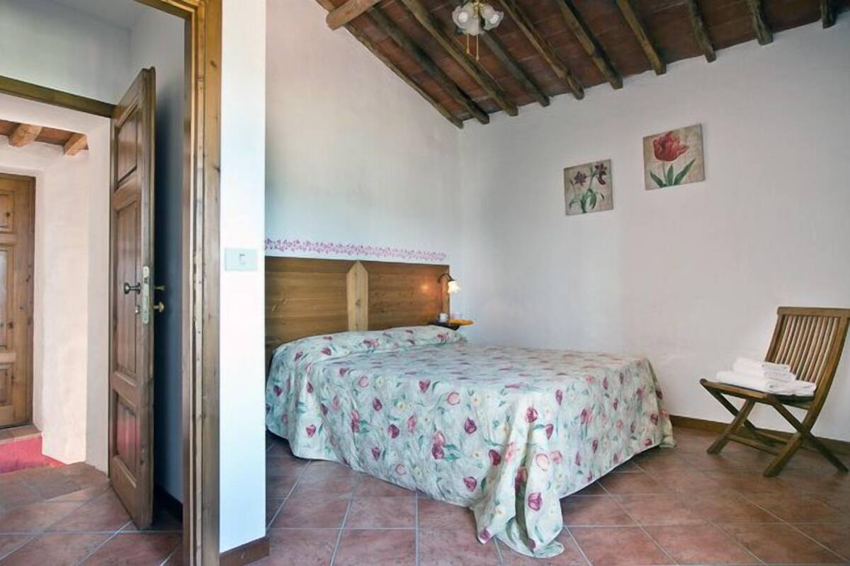 Un dormitorio con cabecera de madera, cama con ropa de cama floral, una silla con toallas y una puerta de madera.