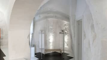A hallway with white walls and a black and white floor pattern, leading to a door.