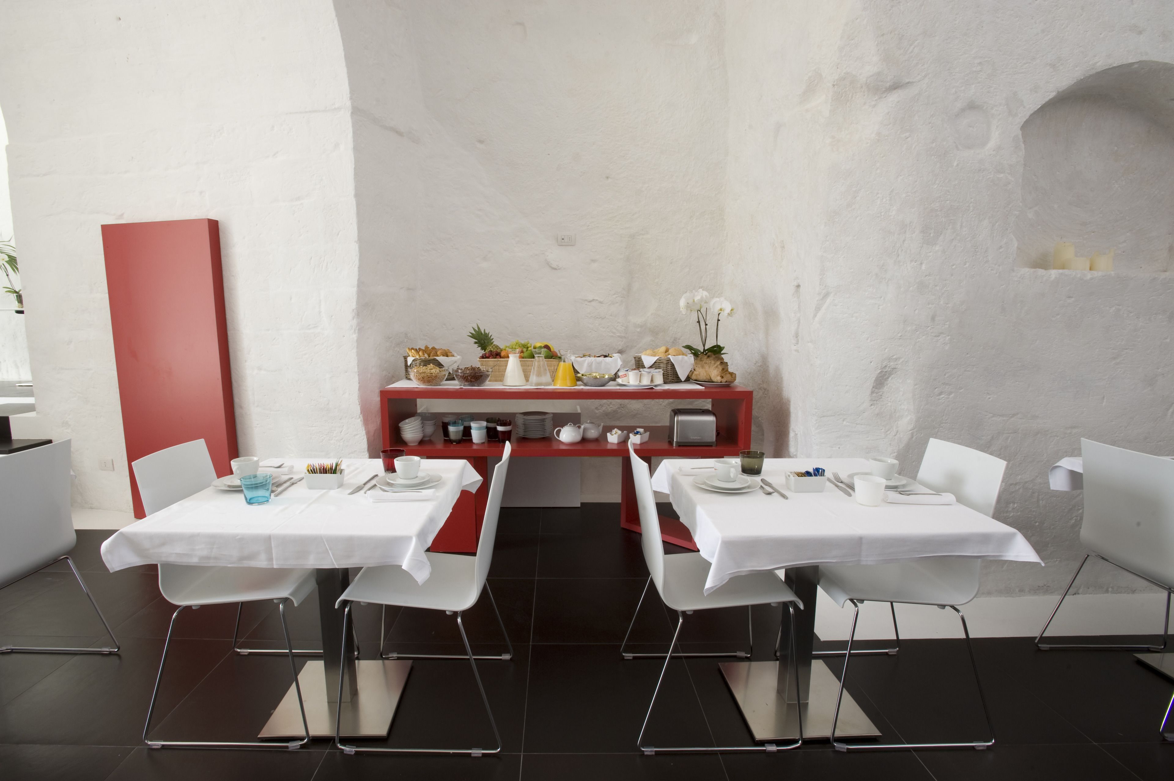 A modern dining area with two tables, white chairs, and a red accent wall.