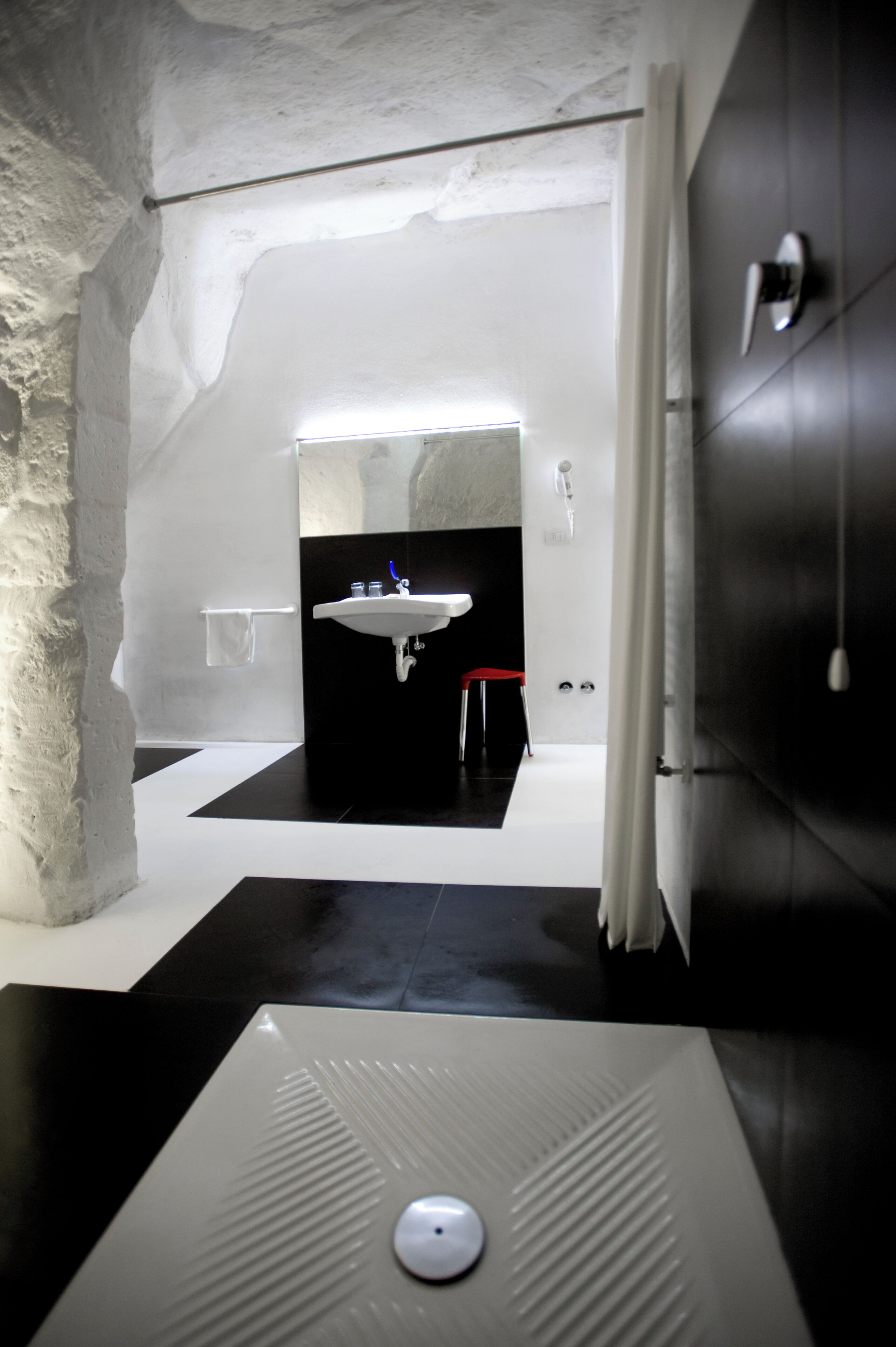 Een moderne badkamer met een zwart-wit vloer, een witte wastafel en een rode kruk.
