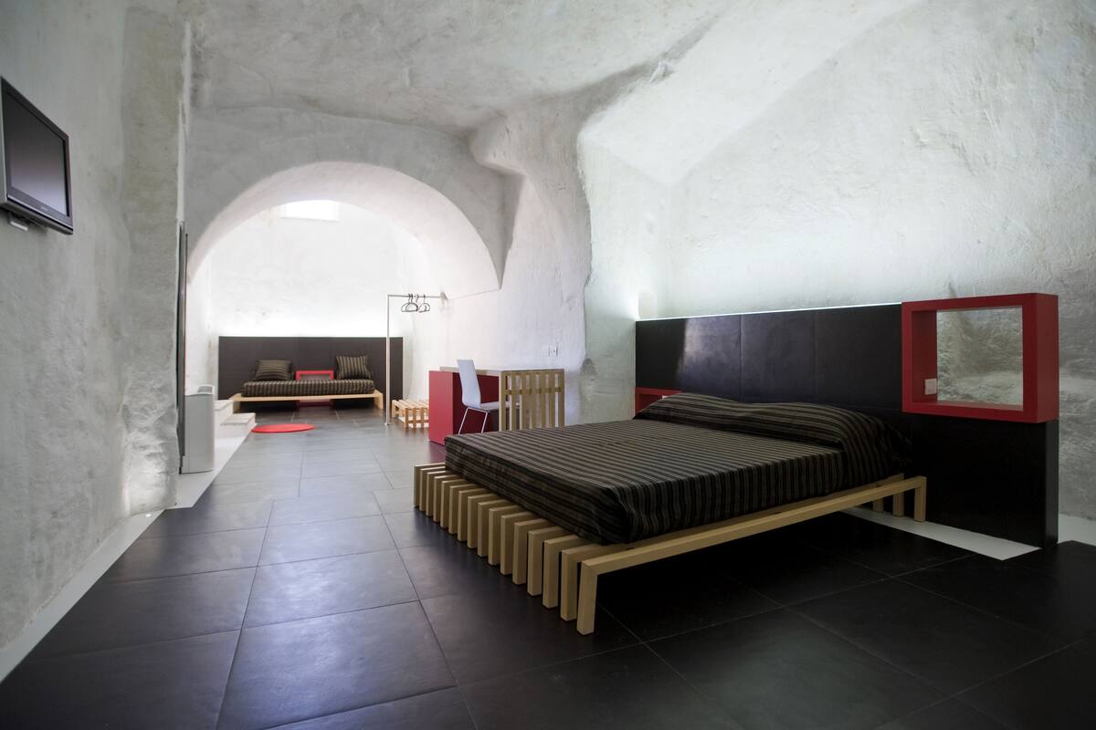 A modern bedroom with a unique arched ceiling, a bed with a wooden frame, a desk, and a chair.