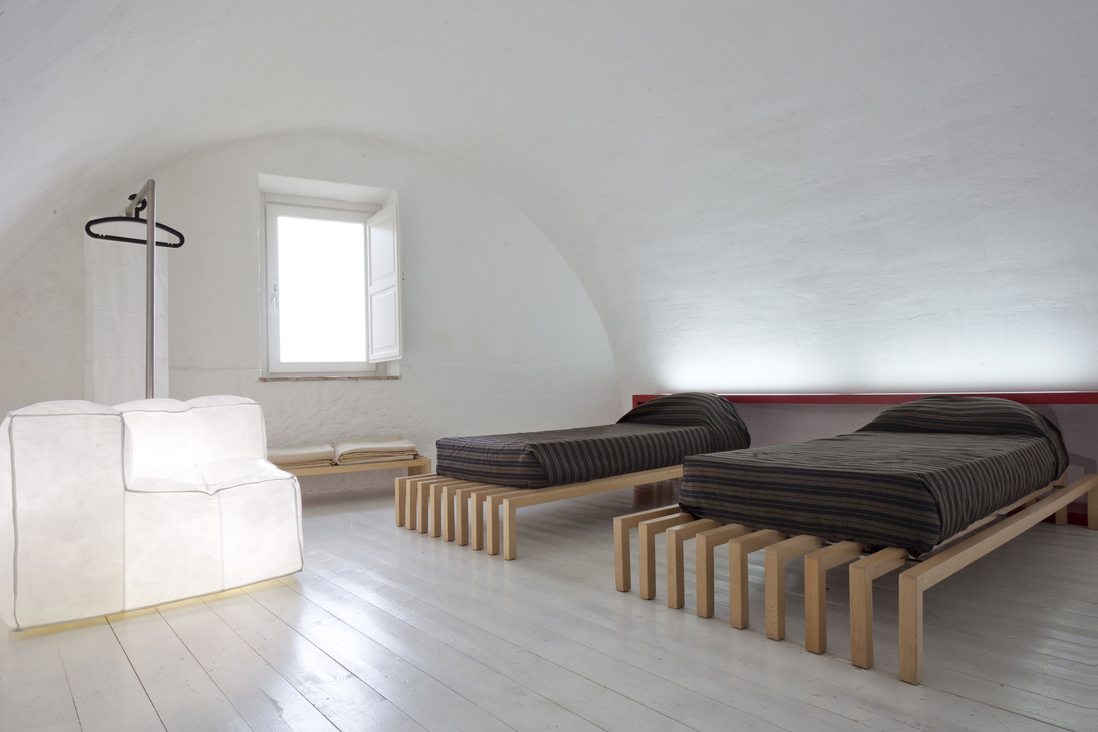 Een minimalistische slaapkamer met twee houten bedden, een witte bank en een raam dat natuurlijk licht binnenlaat.