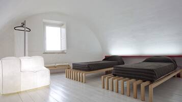 Camera da letto minimalista con due letti in legno, un divano bianco e una finestra che lascia entrare luce naturale.