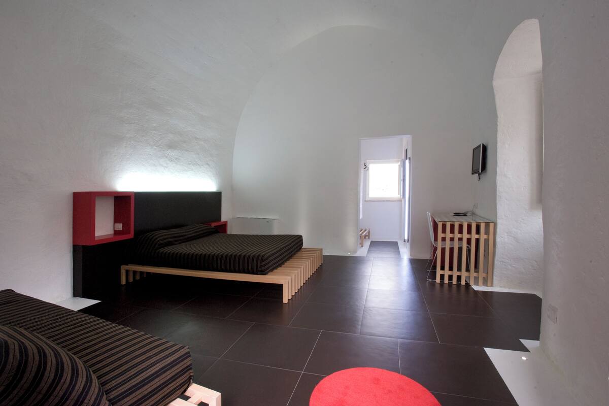 A modern bedroom with a bed, a red shelf, a desk, and a chair.