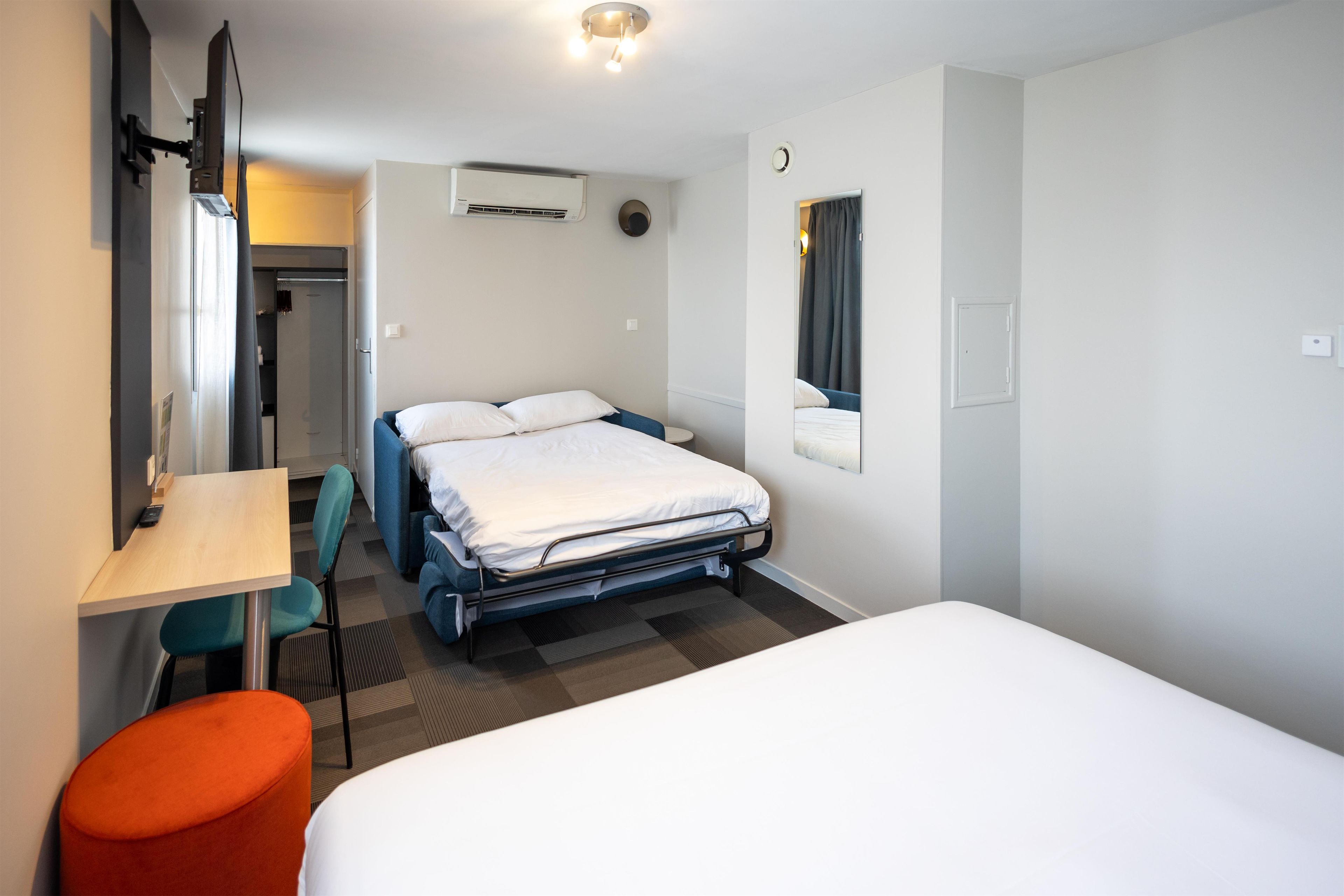 Une chambre d’hôtel comprenant un lit, un bureau, une chaise, une armoire et un miroir.