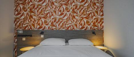 A hotel room with a bed, two bedside lamps, a headboard, and a patterned wall.