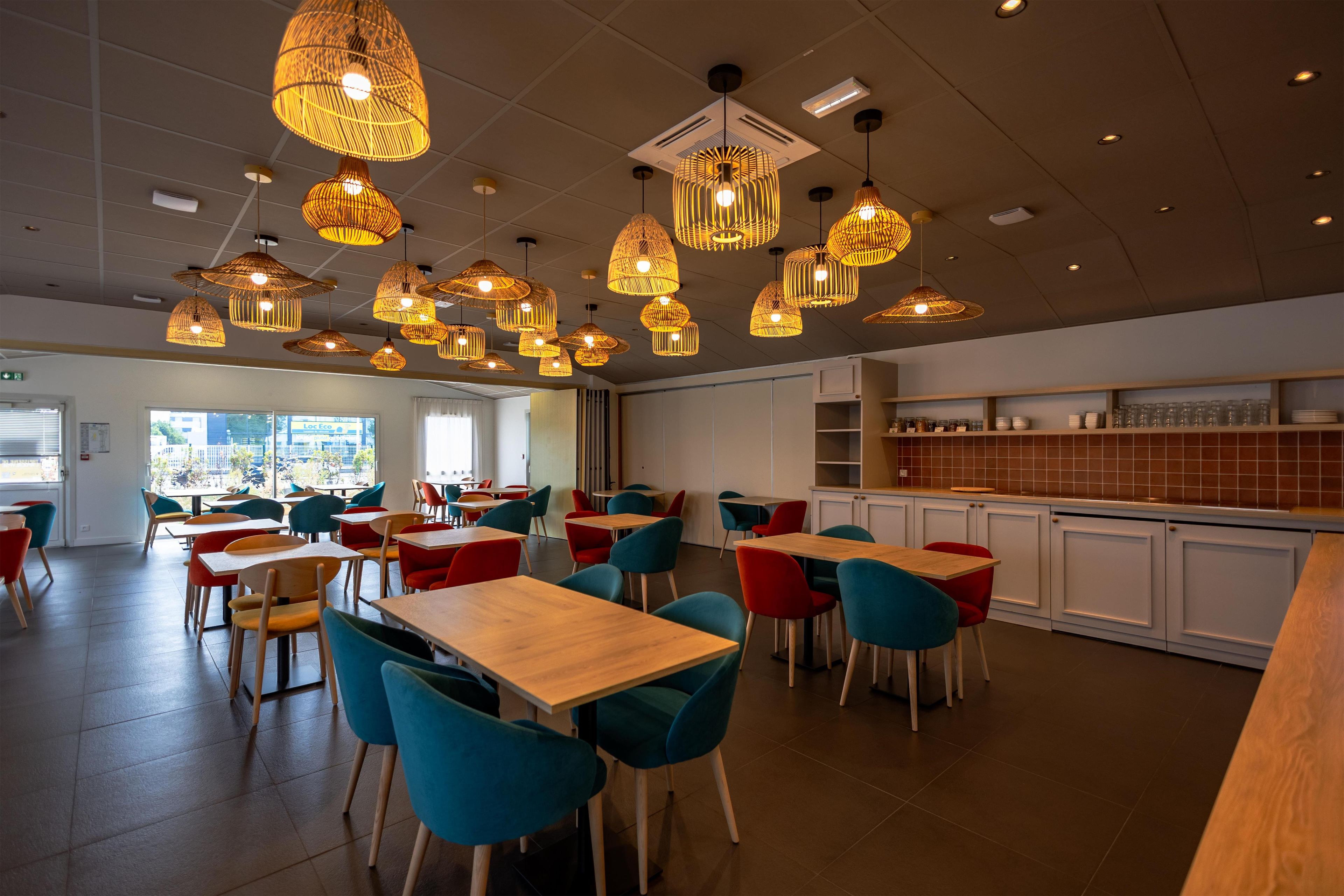 Un restaurante con varias mesas y sillas, iluminación colgante y una zona de cocina.