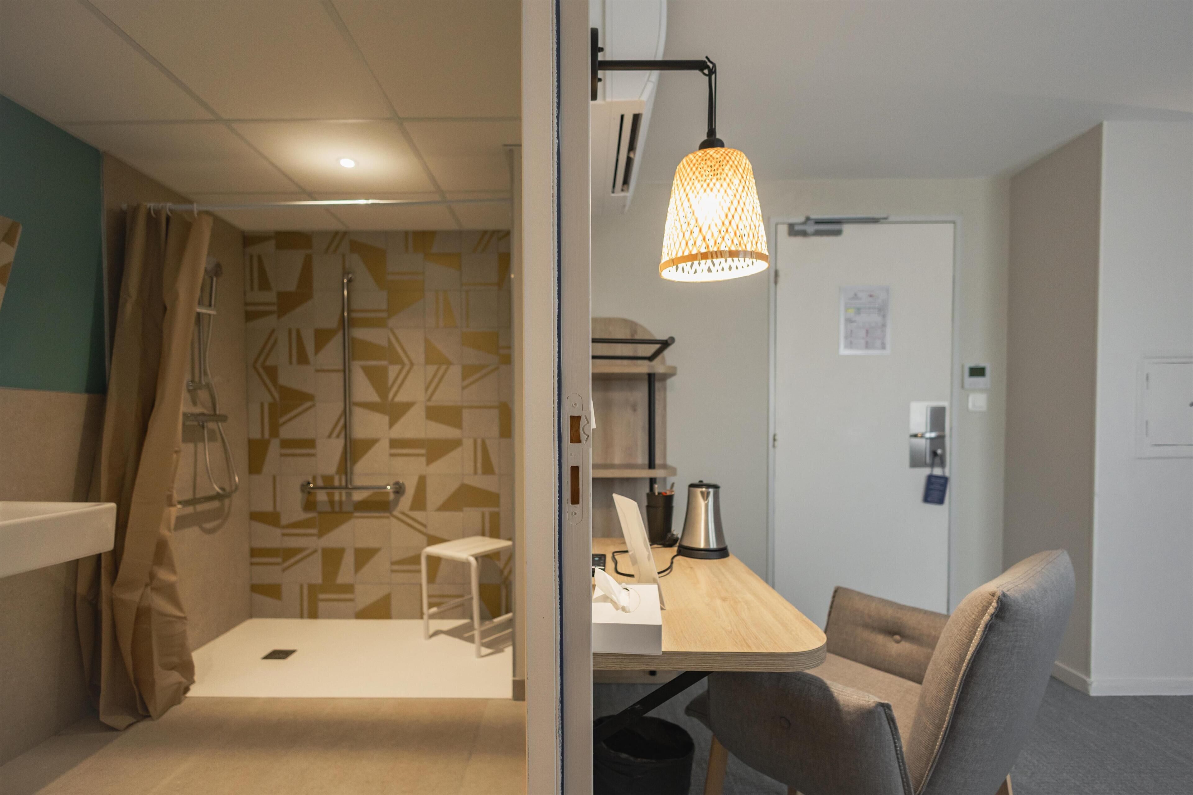 A modern bathroom with a shower, toilet, and sink. There is a wooden desk with a chair and a hanging light fixture.