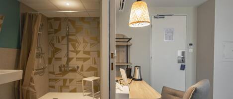 A modern bathroom with a shower, toilet, and sink. There is a wooden desk with a chair and a hanging light fixture.