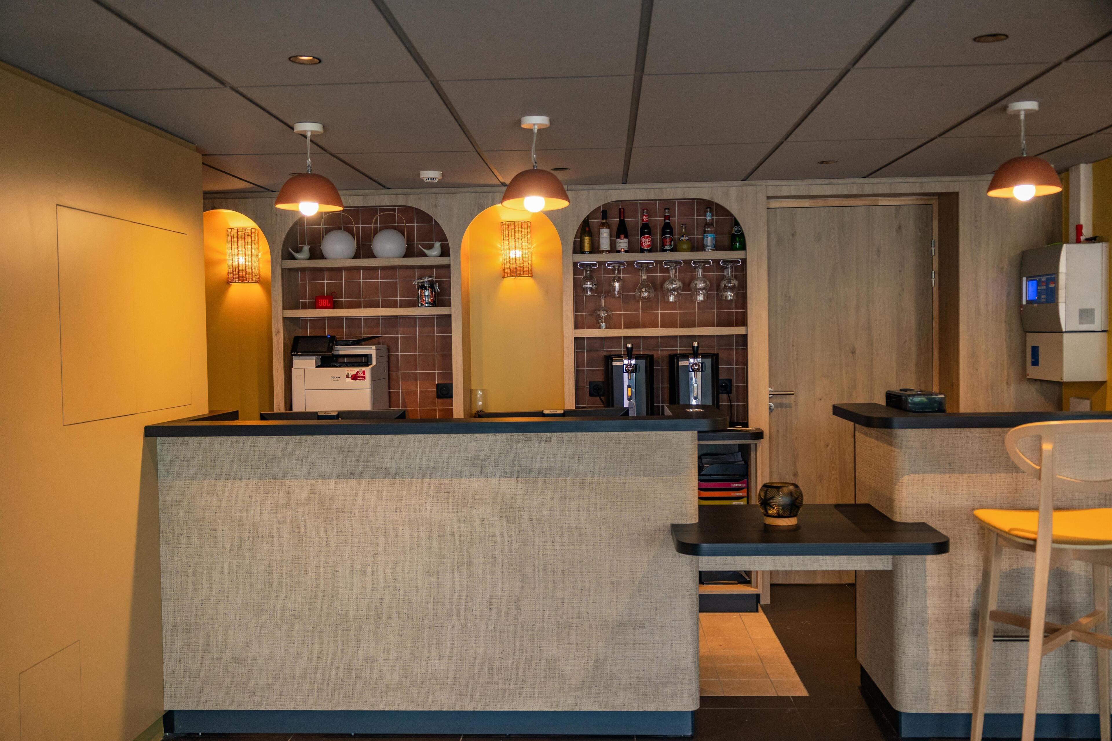Zona de bar con mostrador, asientos y estanterías con botellas y vasos.