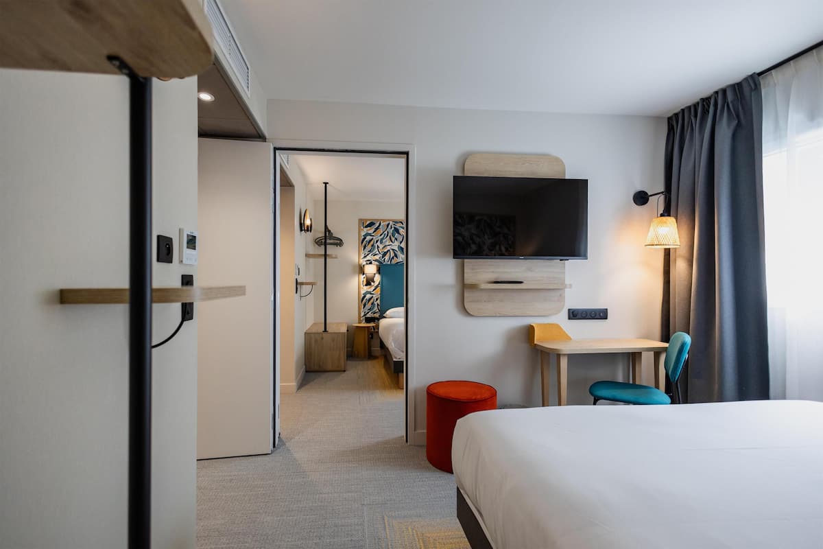 Ein Hotelzimmer mit Bett, Schreibtisch, Stuhl, Fernseher und einem roten Hocker.