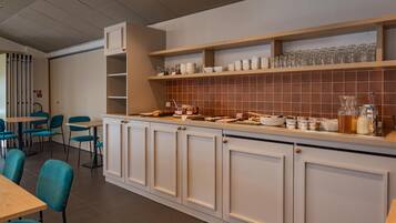 Una cocina moderna con armarios blancos, salpicadero de azulejos y una encimera con diversos utensilios de cocina. Hay sillas azules y una mesa en la zona de comedor.