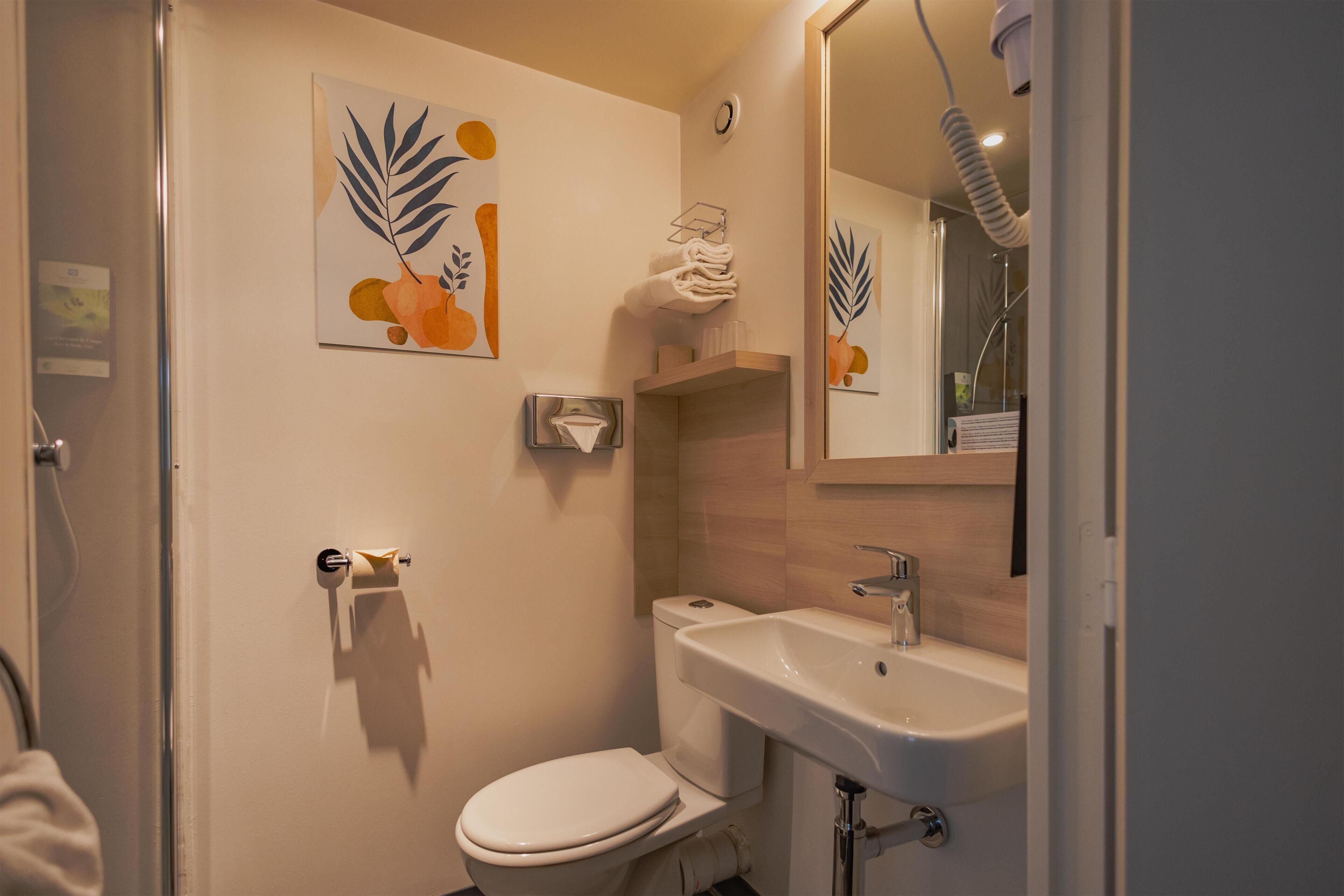 Un baño con inodoro, lavamanos, toallero y espejo.