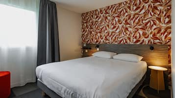 A hotel room with a large bed, a bedside table, a red accent chair, and a patterned wall.