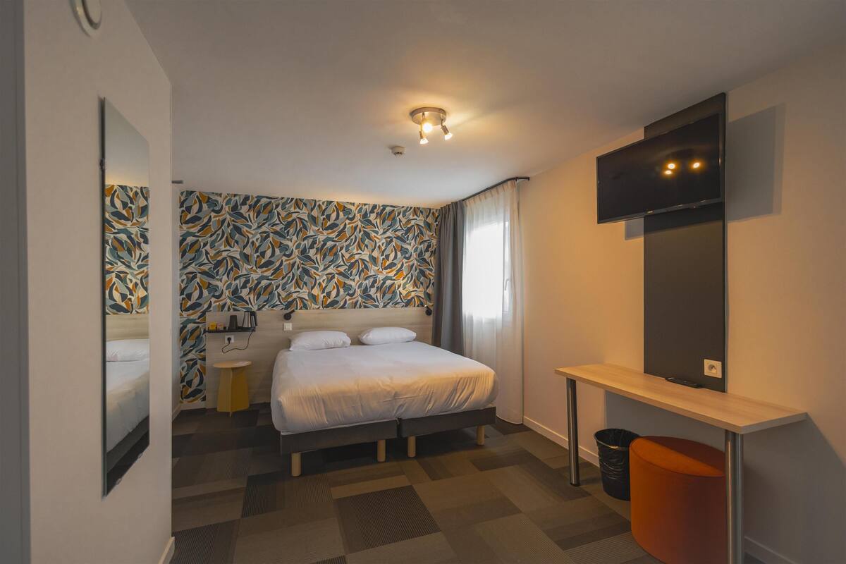 Ein Hotelzimmer mit einem Bett, einem Schreibtisch, einem Fernseher, einem Spiegel und einer Wand mit Muster.