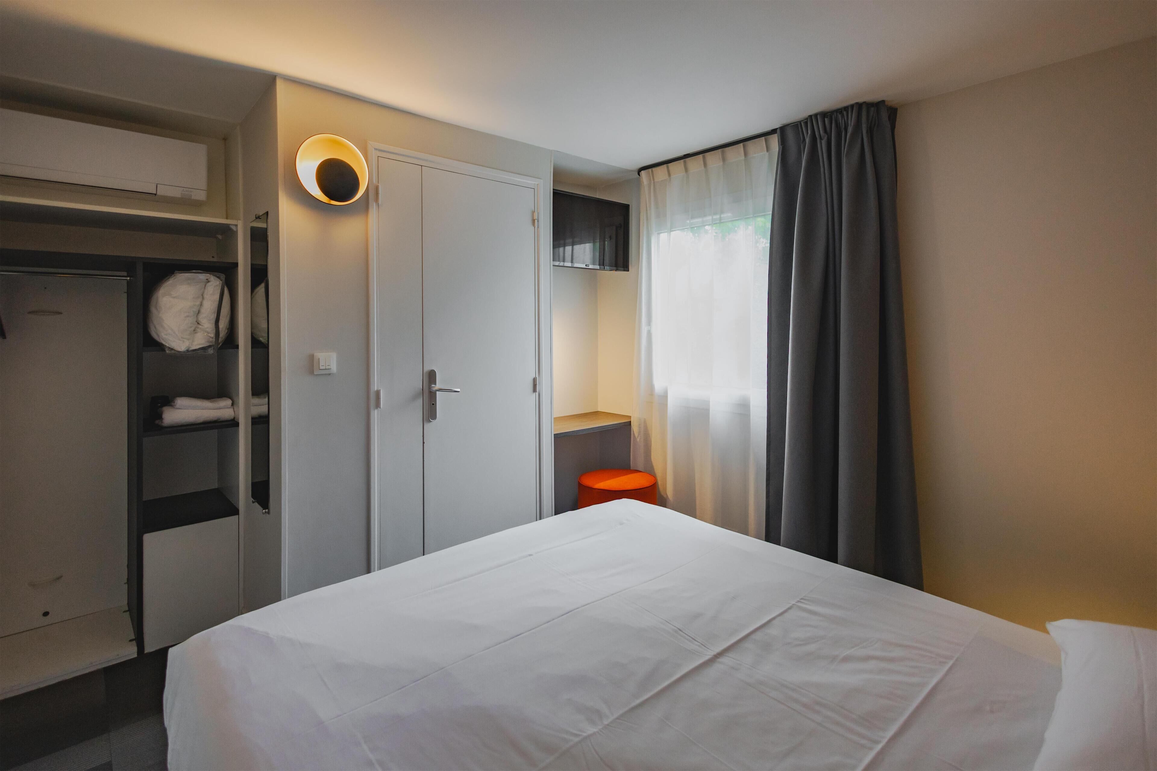 A hotel room with a bed, wardrobe, and a small seating area.