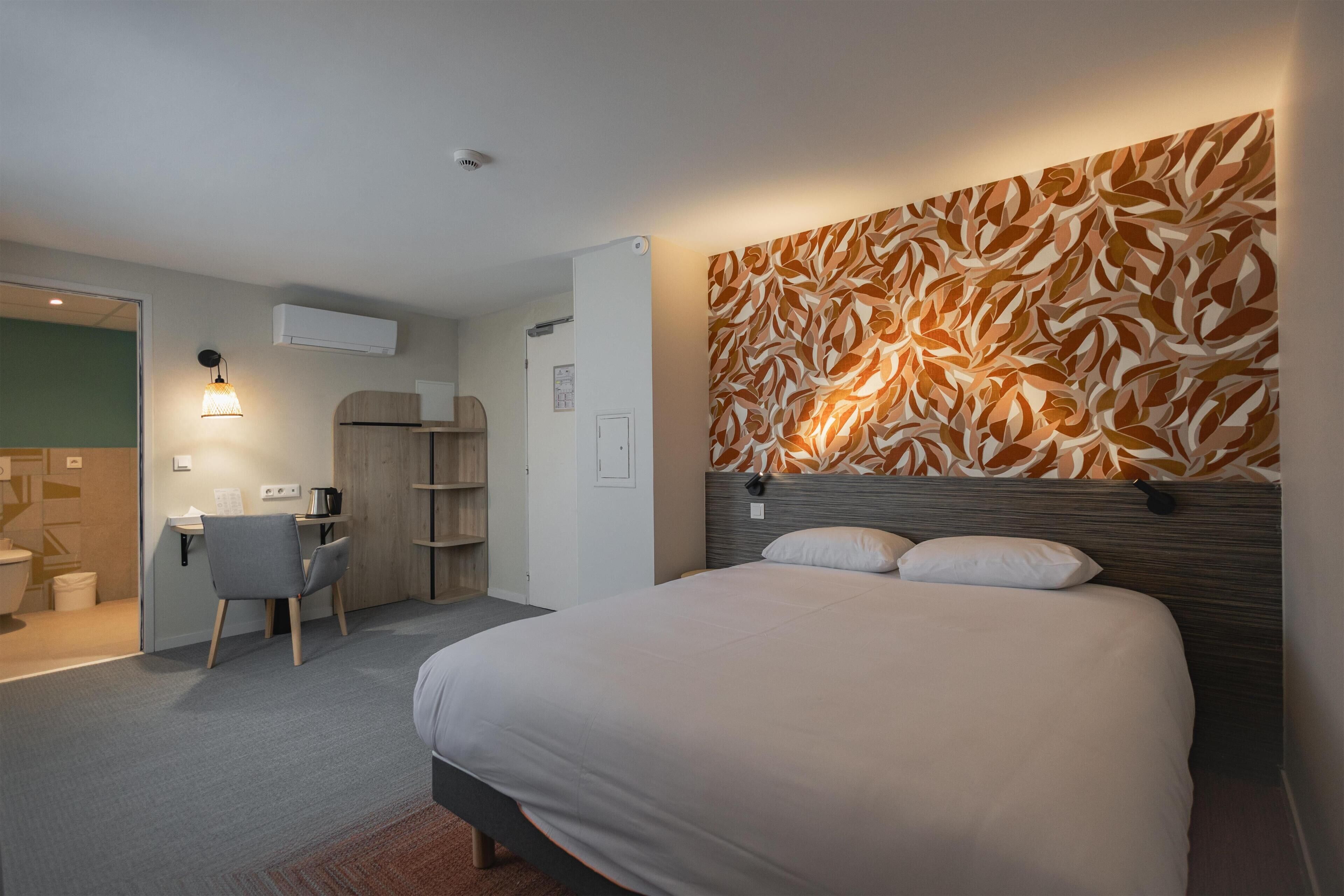 A modern hotel room with a large bed, a desk, a chair, and a bathroom.