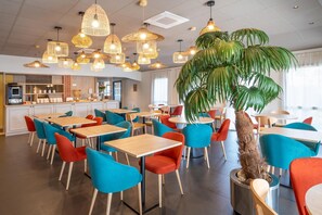 Un café moderne avec de nombreuses tables et chaises, une plante au centre et un bar situé au fond de la pièce.