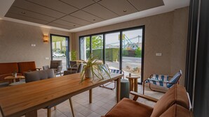 A modern indoor space with a wooden table, seating area, and large windows offering a view of the outside. - Sure Hotel by Best Western Nantes Saint-Herblain (Saint-Herblain)