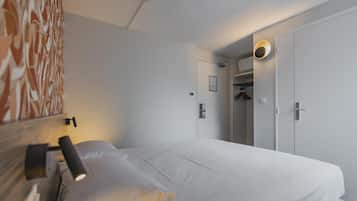 Habitación de hotel con cama, lámpara de noche, luz en la pared, una puerta y un armario.