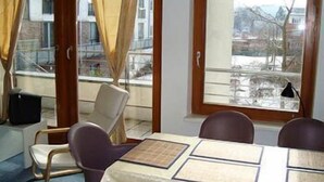 A room with a table set for four, a chair, a lamp, and a view of a snowy landscape through a window. - Apartment Engel (Berlin)