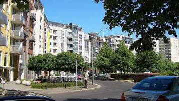 A street view with multi-story residential buildings, parked cars, and trees.