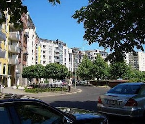 A street view with multi-story residential buildings, parked cars, and trees.