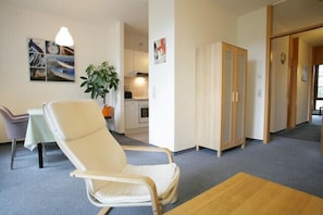A room with a white chair, a small table, a plant, and a wardrobe.