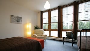 A room with two beds, a chair, a TV, and large windows. - Apartment Engel (Berlin)