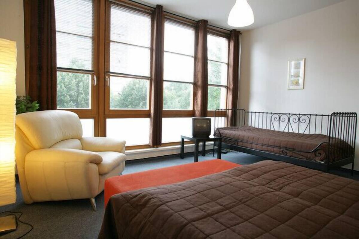 A room with a bed, a chair, a television, and large windows.