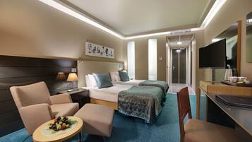 Een hotelkamer met een bed, twee fauteuils, een klein tafeltje met fruit, een bureau met een laptop en een televisie.