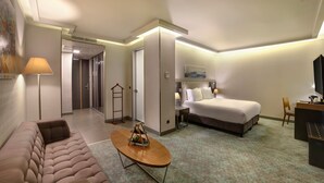 A hotel room with a sofa, a bed, a desk, a lamp, and a painting on the wall. - Divan Corlu (Corlu)