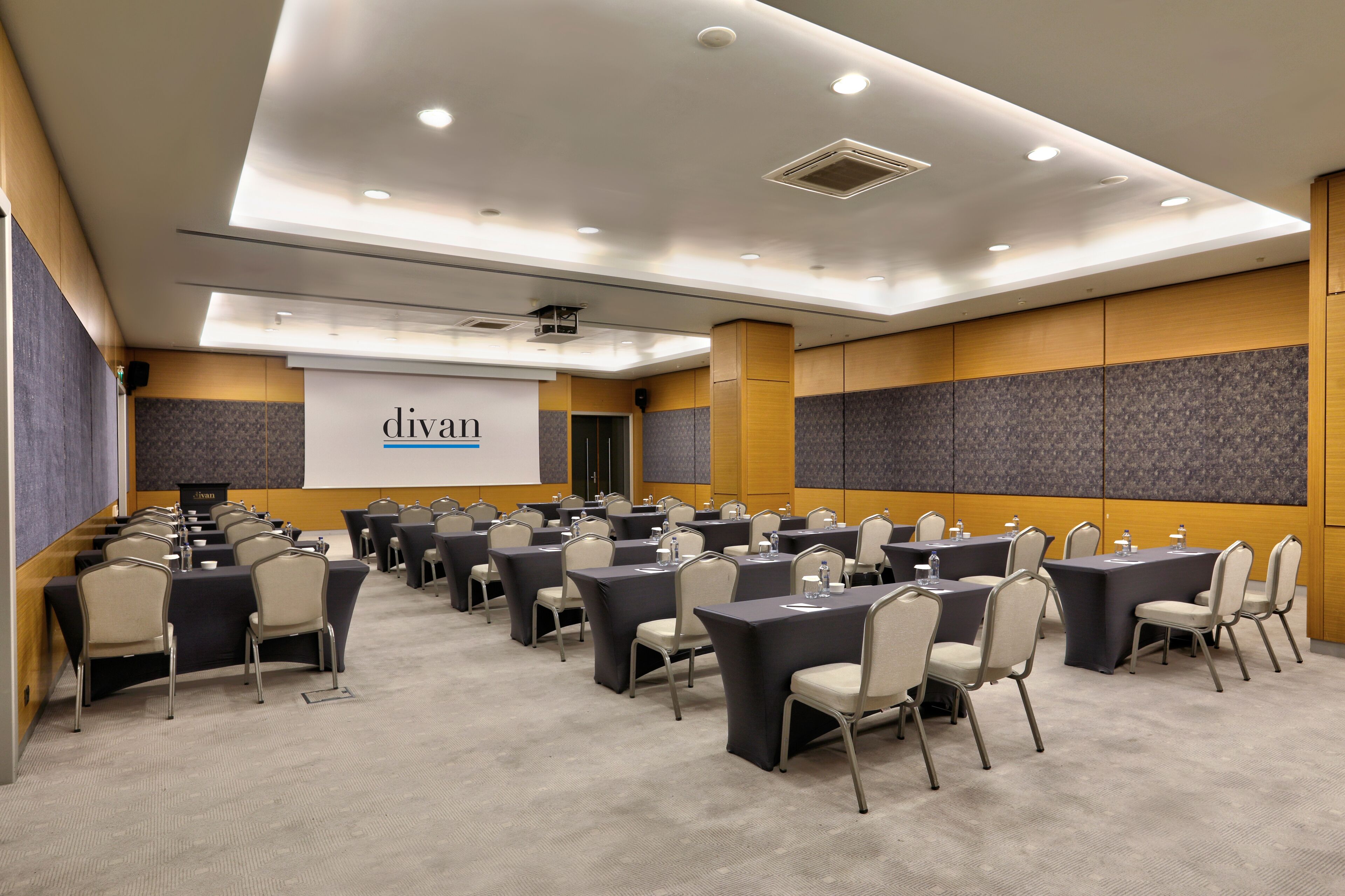 A conference room with multiple tables and chairs, a projector screen, and a podium.