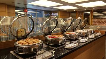 Buffet com diversos alimentos em recipientes tampados, um letreiro com a palavra 'divan' ao fundo e uma parede de tijolos.