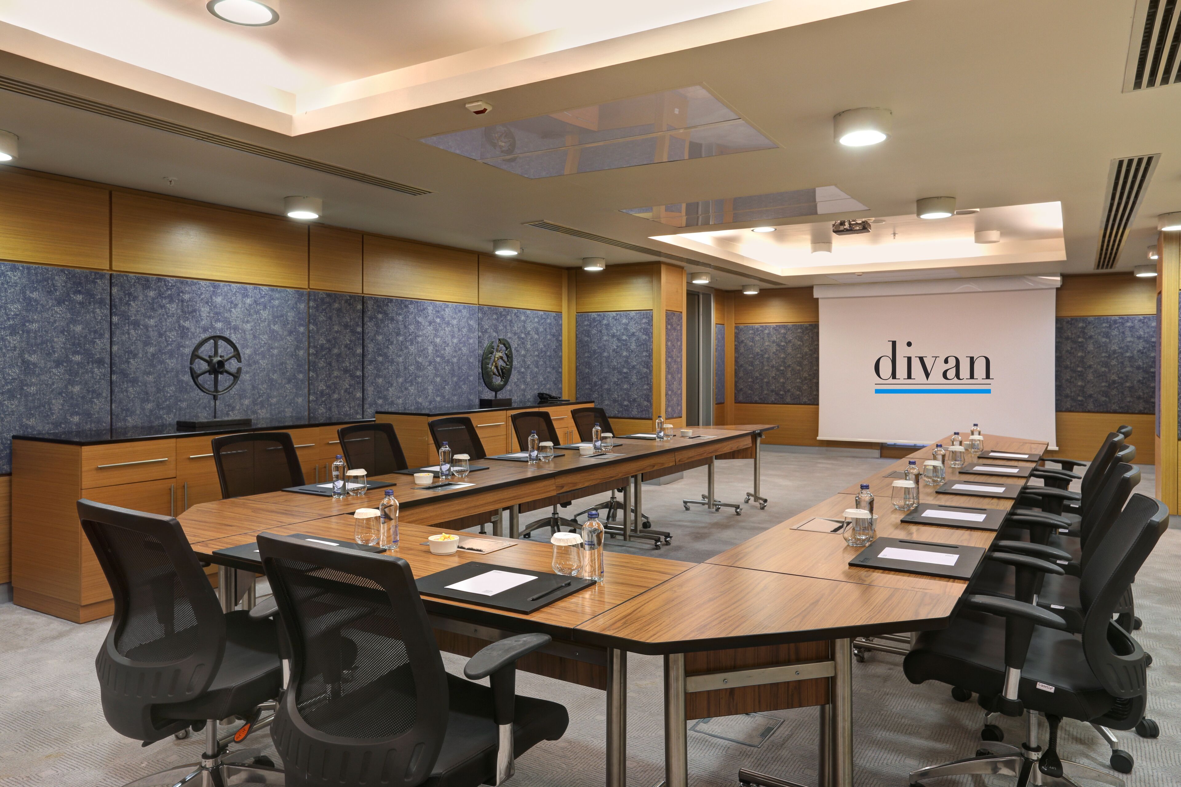 Un salón de conferencias con una larga mesa, sillas y una pantalla de proyector mostrando la palabra 'divan'.