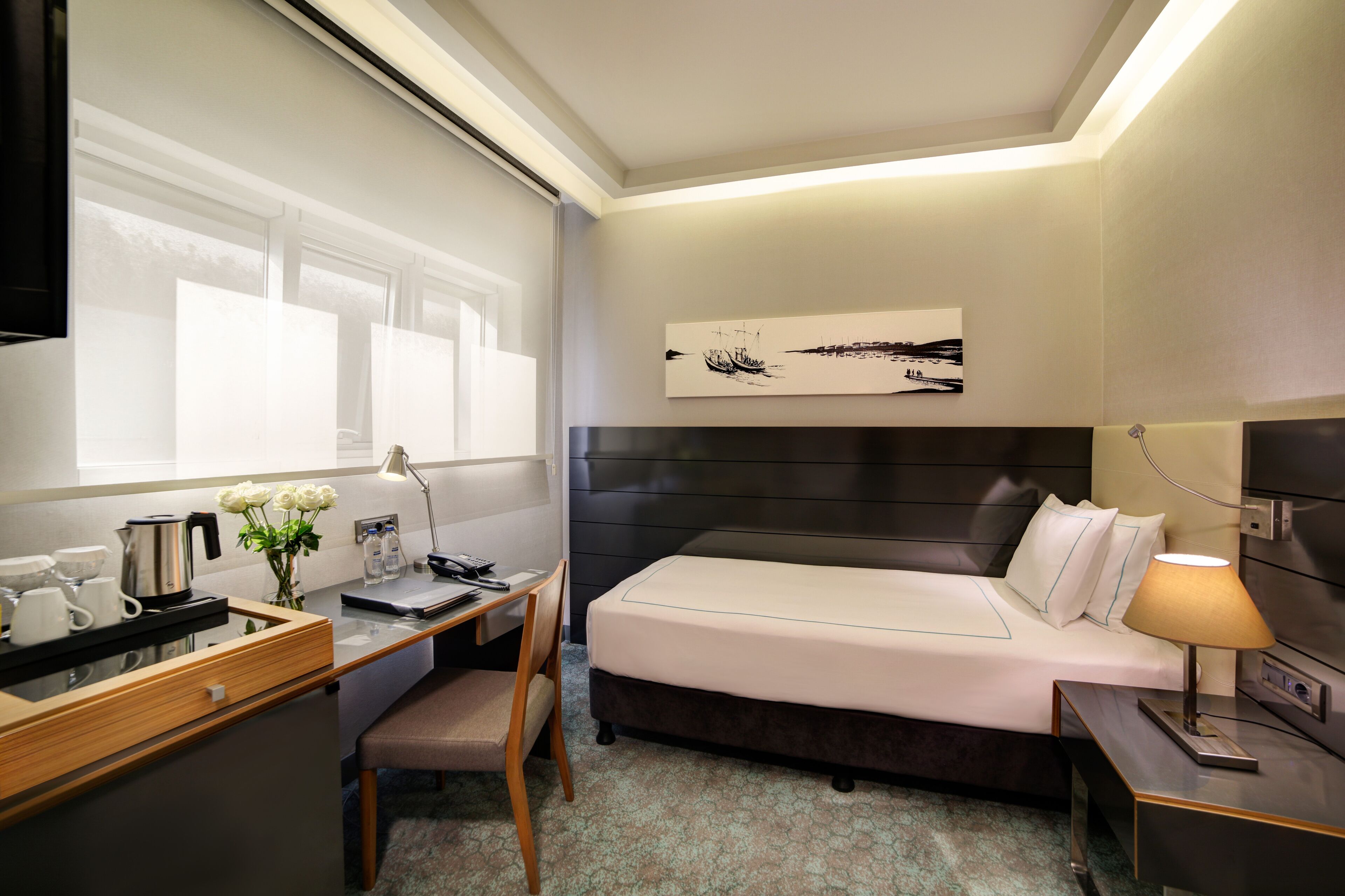 Una habitación de hotel moderna con cama, escritorio, silla y un ventanal grande.