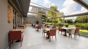 A modern dining area with multiple tables and chairs, large windows offering a view of the outdoors, and a contemporary interior design. - Divan Corlu (Corlu)