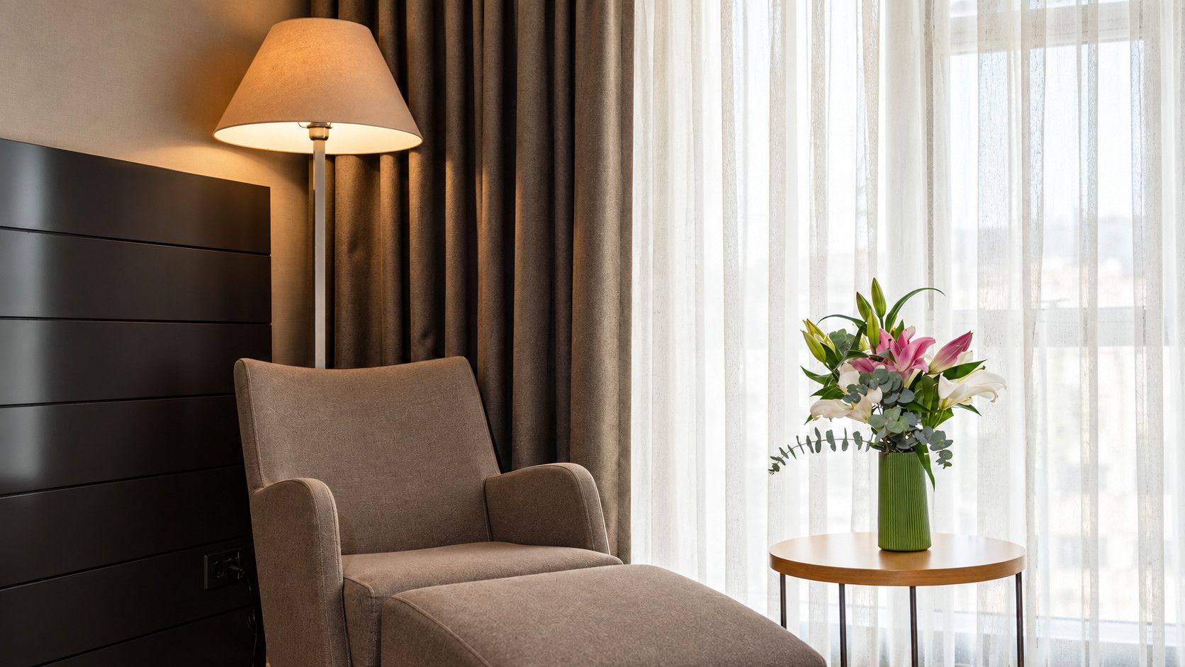 A modern room with a dark-colored sofa, a floor lamp, and a vase with flowers on a small table.
