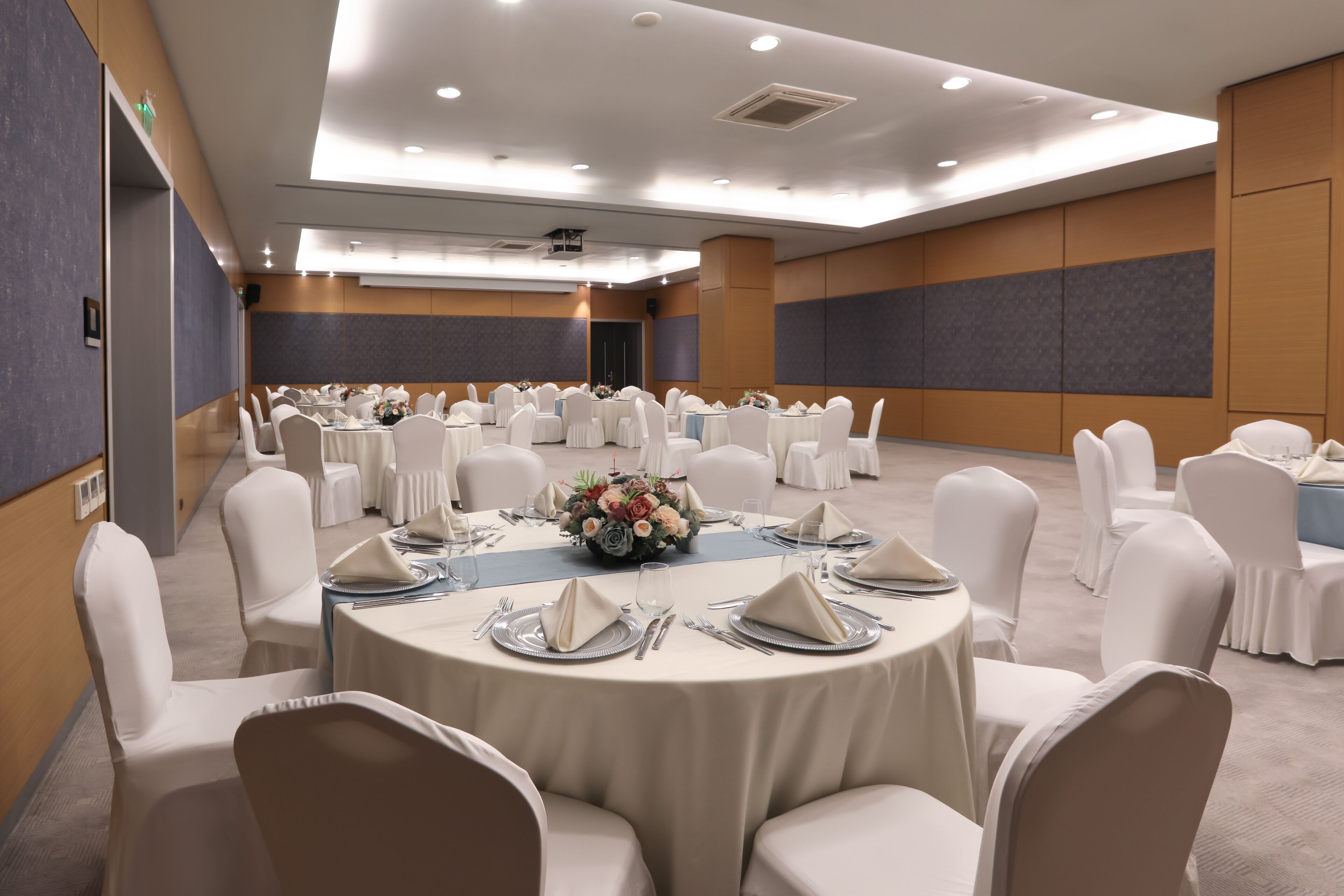 Una sala de conferencias con mesas redondas, sillas blancas y centros de mesa florales.
