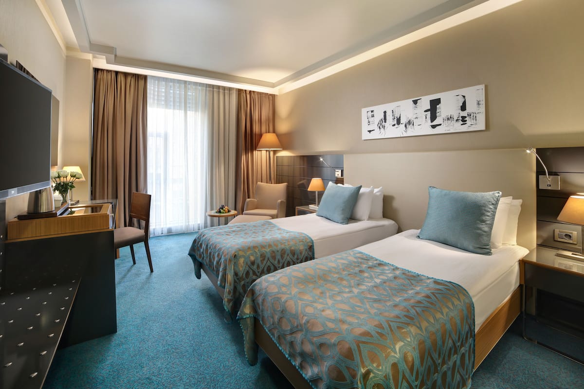 A hotel room with two beds, a desk, a chair, a TV, and a window with curtains.