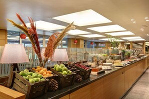 A buffet with various fruits and vegetables, including apples and oranges, and decorative plants.