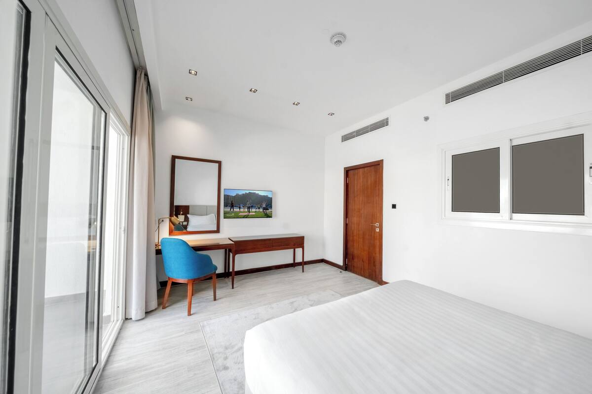 Una habitación de hotel moderna con una cama grande, un escritorio con una silla, una ventana y una puerta.