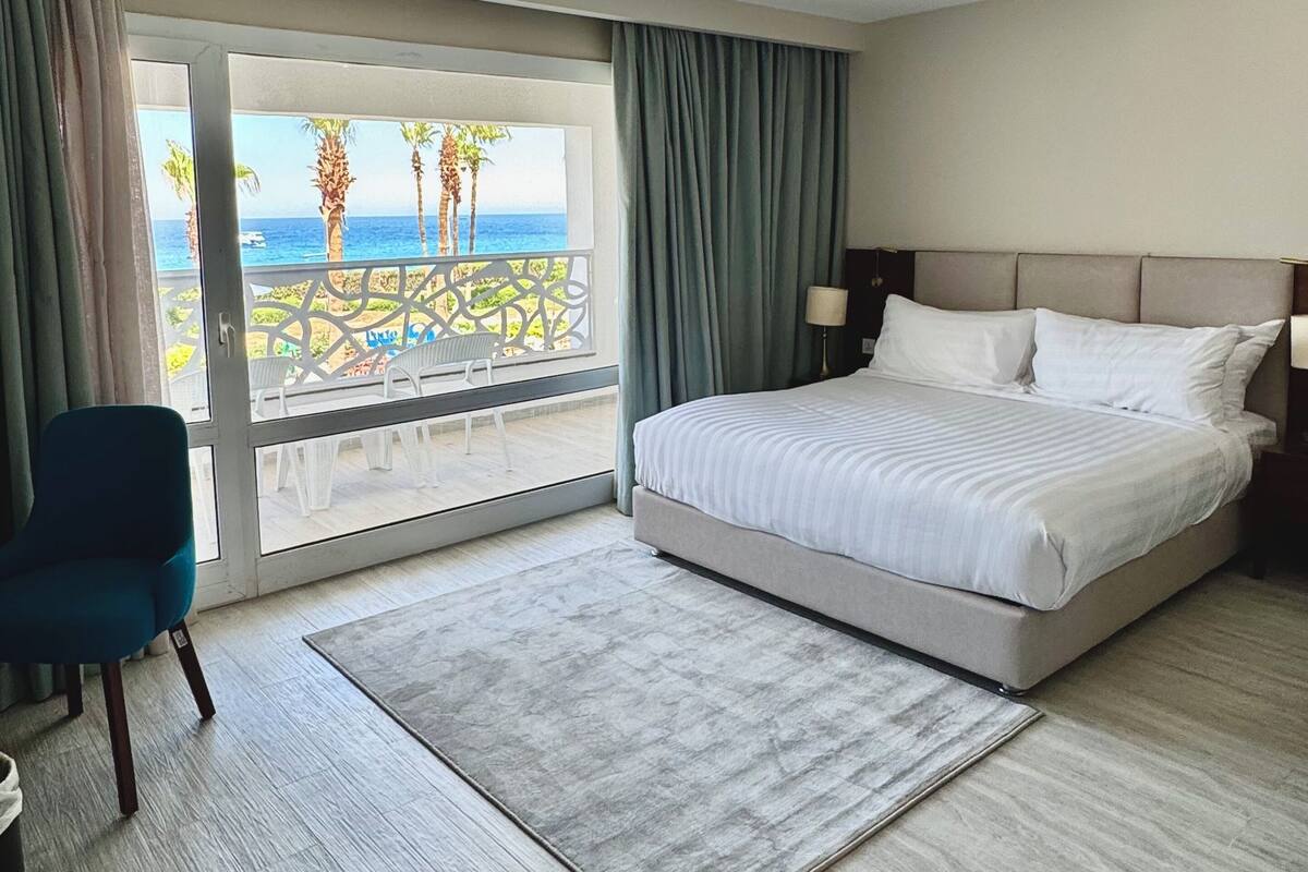 Habitación de hotel con una cama grande, una silla, vista al océano y un balcón.
