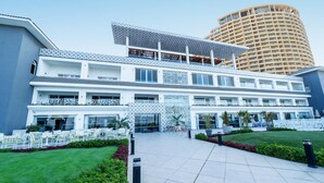 A modern hotel with a spacious outdoor area, multiple balconies, and a large building in the background.