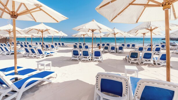 A beach with rows of white lounge chairs and large white umbrellas.