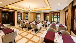A hotel dining area with multiple tables, chairs, and a chandelier.