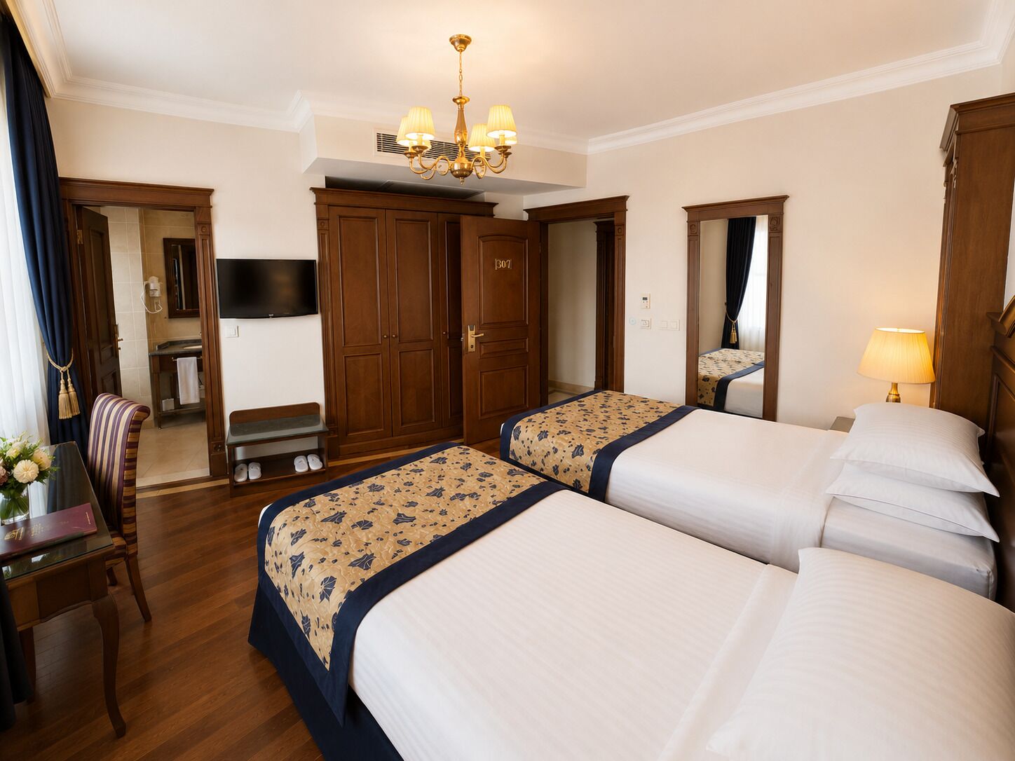Une chambre d’hôtel avec deux lits, un bureau, une chaise, une télévision et un lustre.