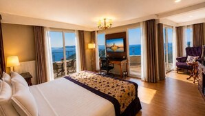 A hotel room with a large bed, a desk, a chair, a purple armchair, and a TV.